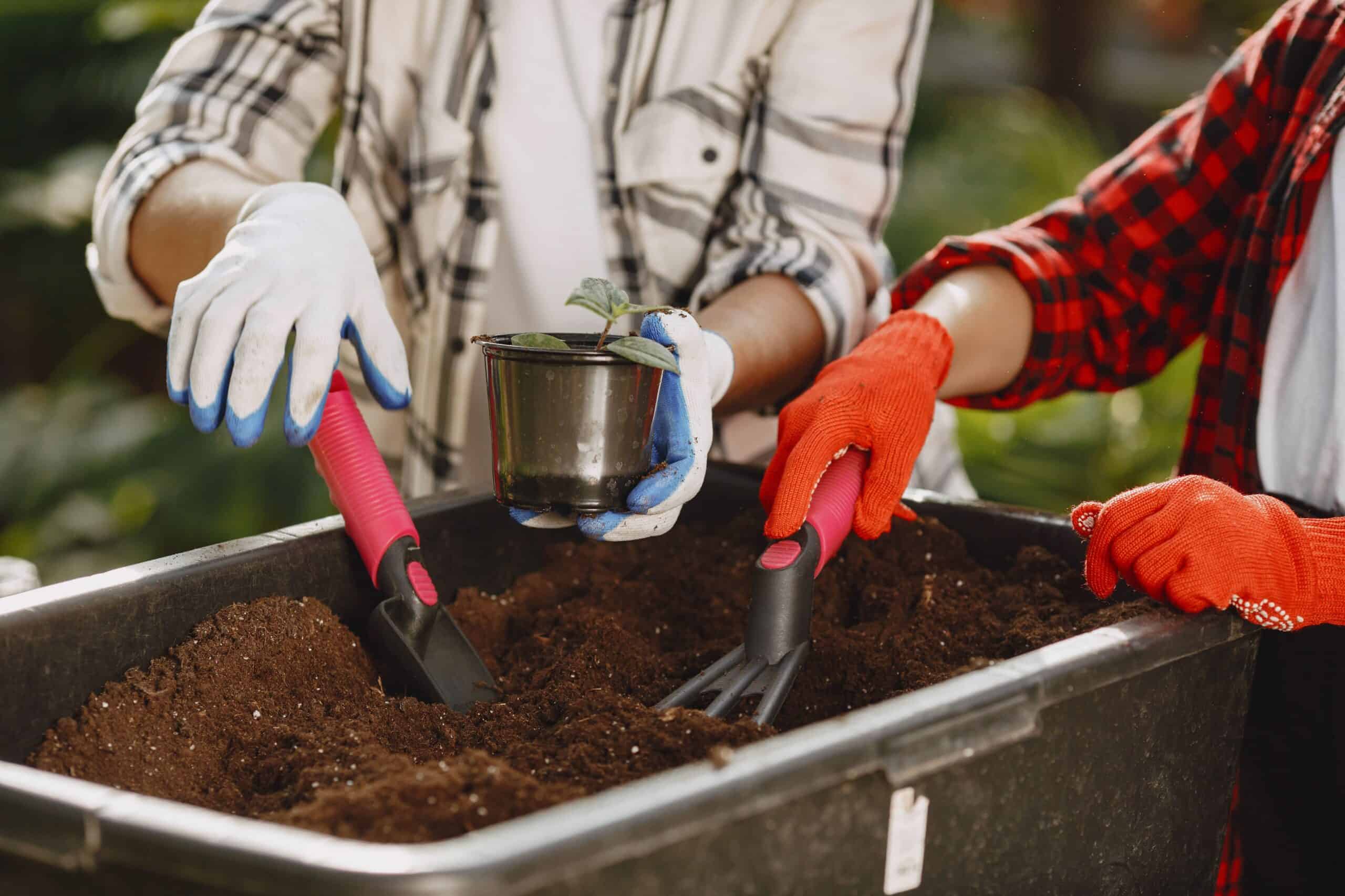 Two people scooping and mixing garden soil by hand with a trowel