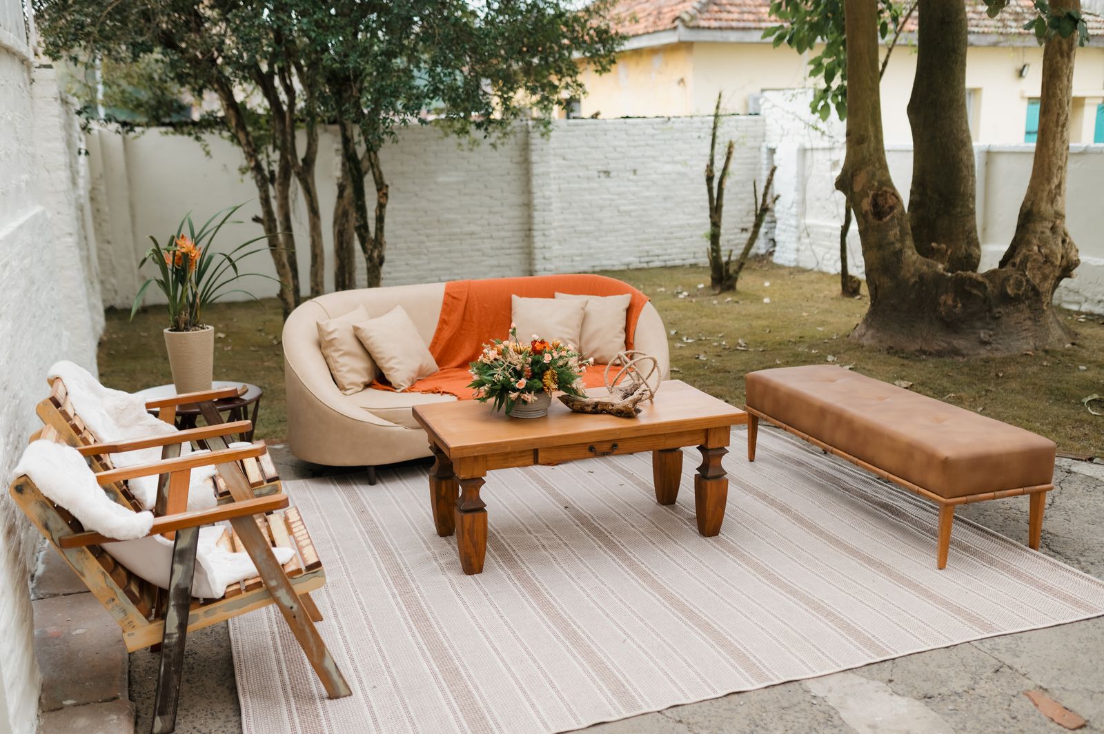 A small walled backyard patio with a rug, low coffee table, sofa, and armchairs arranged as one defined seating zone
